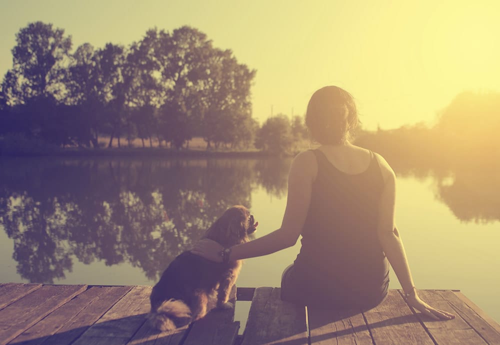 Vintage photo of young woman relaxing with her dog at the lake in sunset